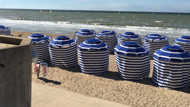 Een strand met gestreepte strandparasols en een betonnen looppad.