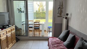 Een woonkamer met een bank, een televisie en een schuifdeur naar een terras.