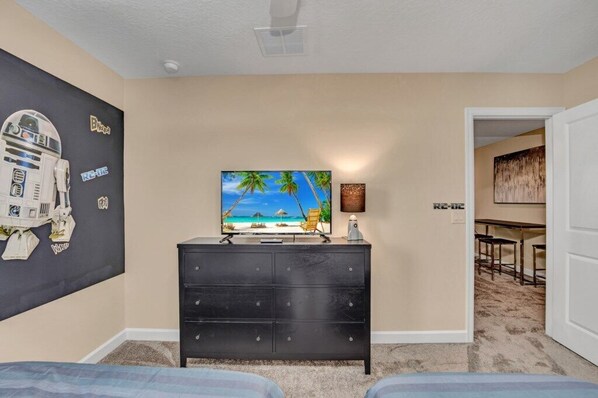 Una habitación con decoración de playa, un televisor de pantalla plana, un aparador negro y un acceso a otra habitación.