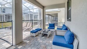 Un espace extérieur aménagé, abrité et doté de mobilier en osier et de coussins bleus, de grandes fenêtres et d’une vue sur les bâtiments environnants.