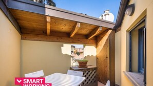 A patio area with a table and chairs, a wooden pergola, and a view of buildings in the background.