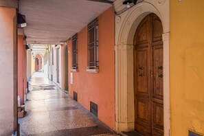 Un couloir avec une porte en bois et des fenêtres, qui mène à un bâtiment dont le mur est jaune.