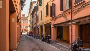 A narrow street lined with parked scooters and classic buildings with arched doorways and shutters.