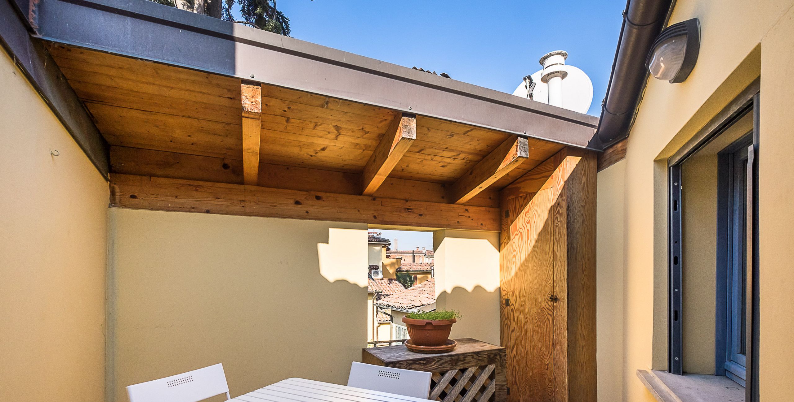 Een patio met een tafel en stoelen, een houten pergola en een uitzicht op gebouwen in de verte.
