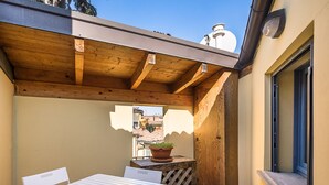 Un espace patio avec une table et des chaises, une pergola en bois et une vue sur les bâtiments en arrière-plan.