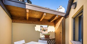 Ein Patio mit Tisch und Stühlen, einer Holzpergola und Blick auf Gebäude im Hintergrund.