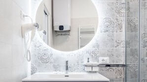 A modern bathroom with a vanity, a round mirror, a towel dispenser, and patterned tiles. - Galleria del Reno 2B by Wonderful Italy (Bologna)