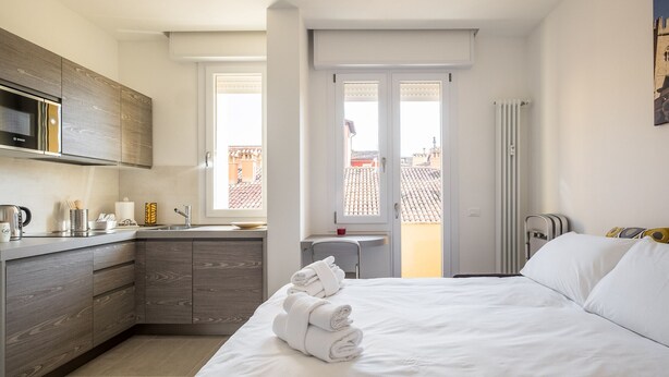 A modern hotel room with a bed, a kitchen area, and a view of the city. - Galleria del Reno 2B by Wonderful Italy (Bologna)