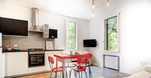 Une cuisine moderne avec un coin repas, un téléviseur fixé au mur et une grande fenêtre offrant une vue sur la verdure.