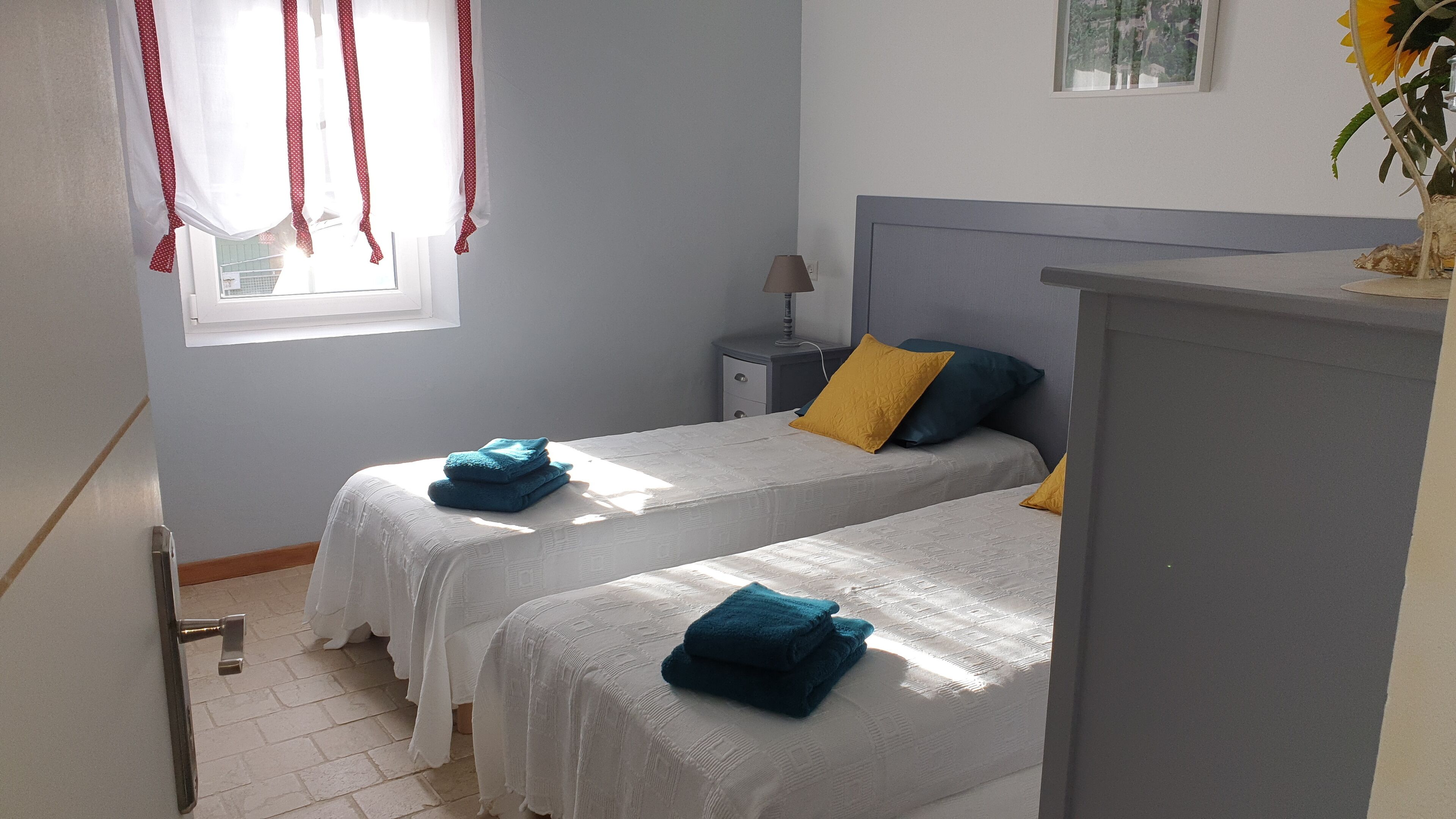 A bedroom with two beds, a nightstand, a lamp, and a window with curtains.