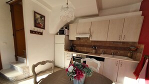 Un comedor con mesa, sillas y un jarrón de flores. Se observa una cocina con armarios y un microondas.