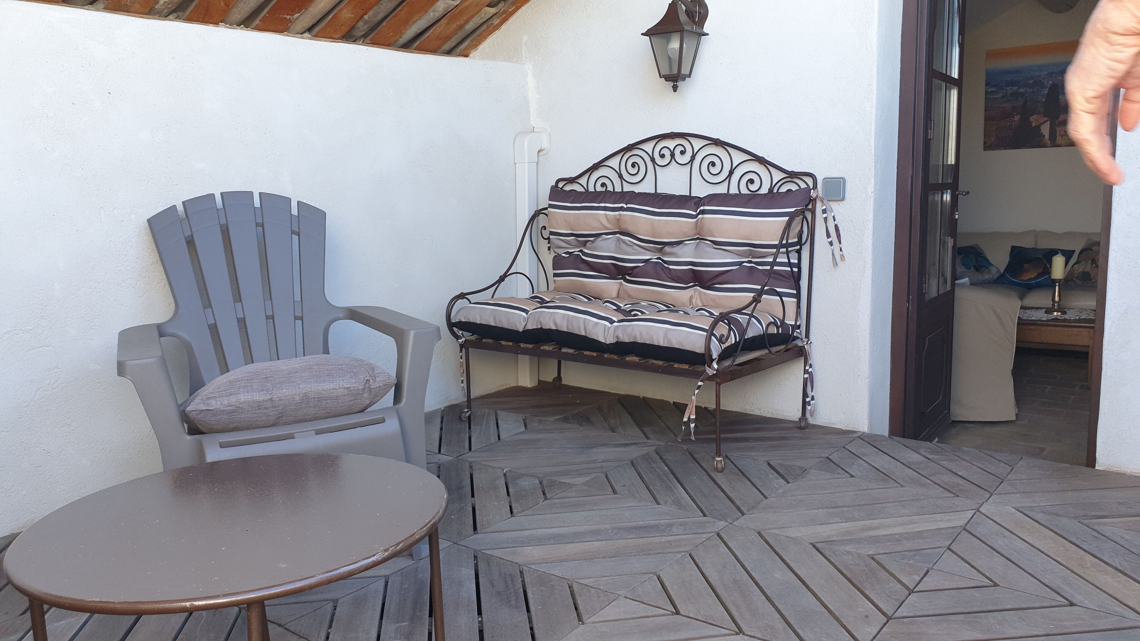 A patio with a metal bench, a plastic chair, and a small round table.