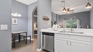 A modern kitchen with white cabinetry, a dishwasher, and pendant lighting.