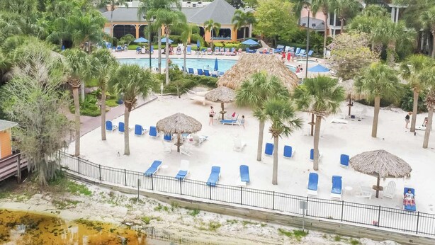 A resort with a pool area, lounge chairs, palm trees, and a small building.