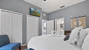 A bedroom with a large bed, two white doors, a blue bench, and a ceiling fan.