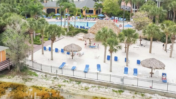 Een resort met een zwembad, ligbedden, palmbomen en een klein gebouw.
