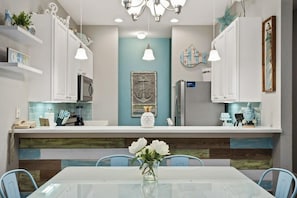 Una cocina moderna con gabinetes blancos, una isla central y un área de comedor con mesa y sillas de vidrio.