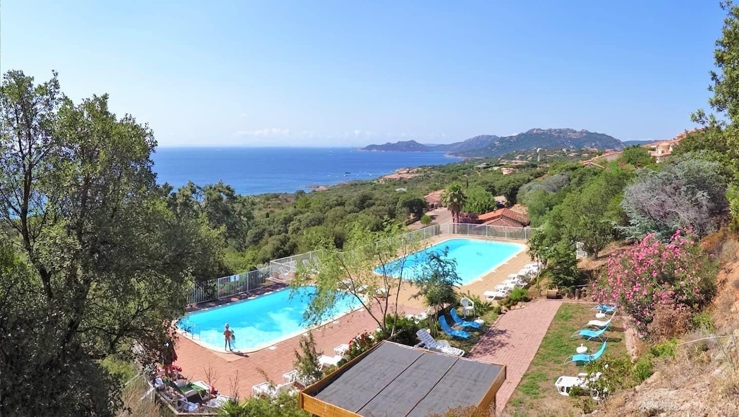 Um resort com duas piscinas, área de praia e vista para o mar e as colinas.