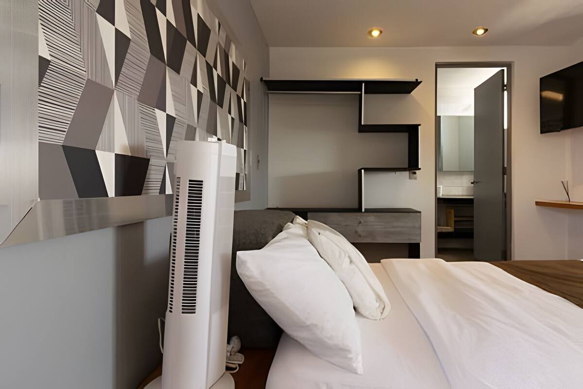 Um quarto moderno com uma cama, um purificador de ar branco, um design geométrico na parede, um guarda-roupa embutido e um espelho.