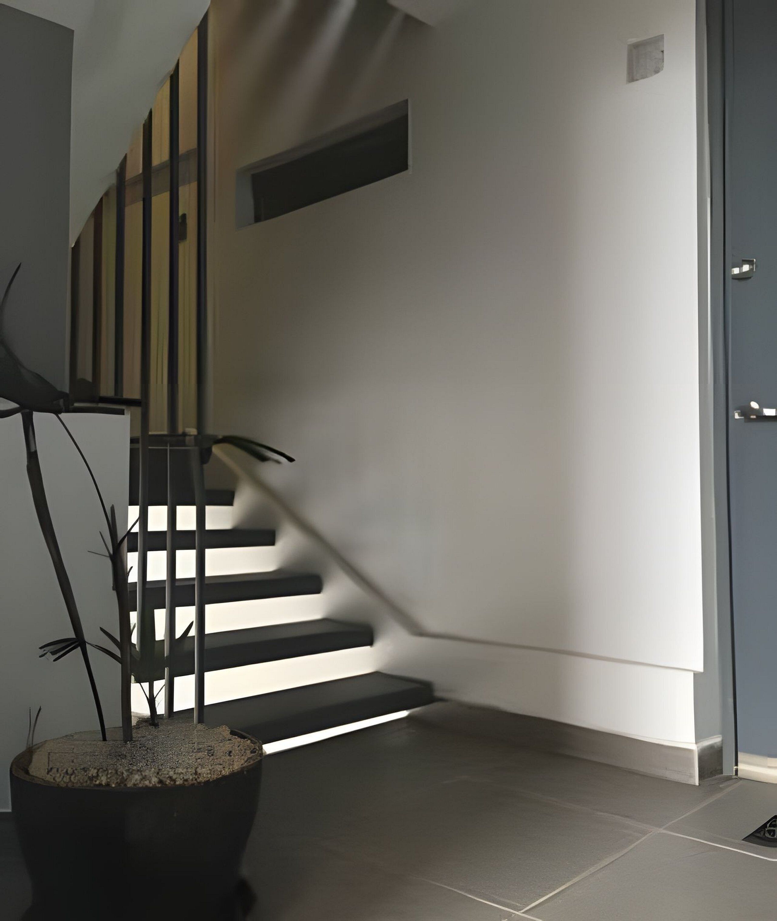 Una escalera moderna de diseño minimalista, una planta en maceta y una puerta a la derecha.
