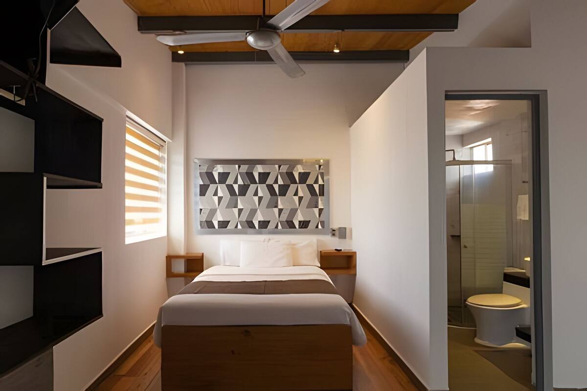 Quarto moderno com cama, uma obra de arte geométrica na parede e área de chuveiro.