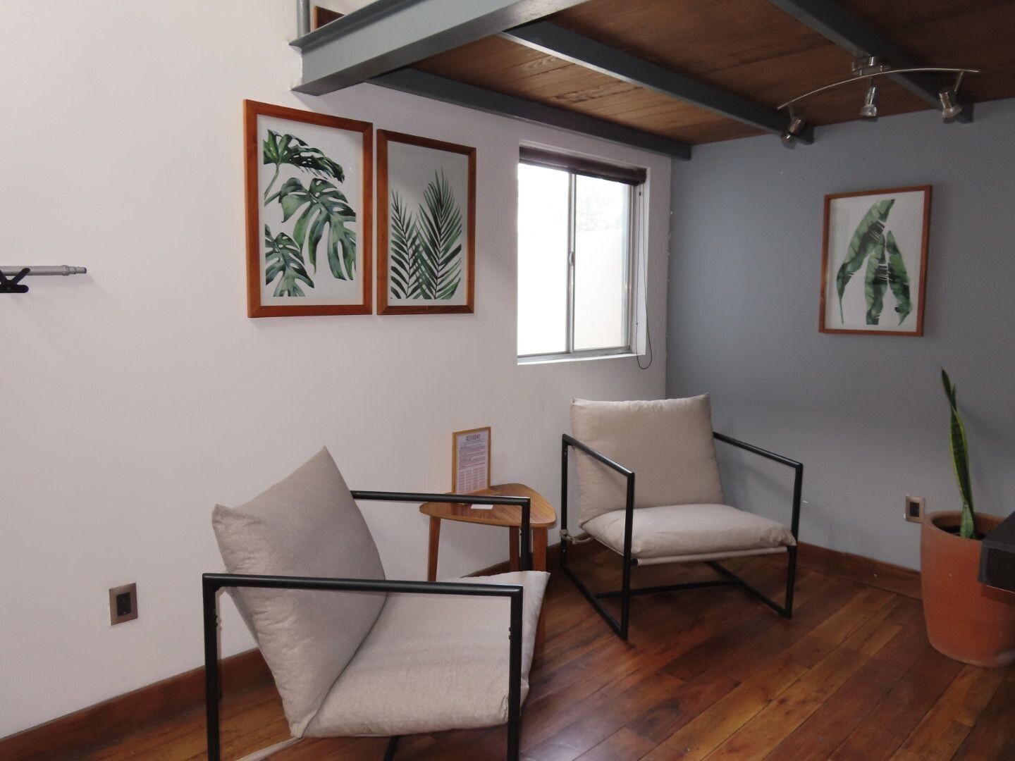 A room with wooden flooring, two armchairs, a small table, and framed botanical prints on the wall.