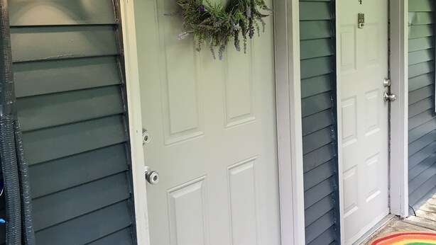 Una casa con puerta blanca, el número 5, un adorno de puerta y un felpudo colorido.