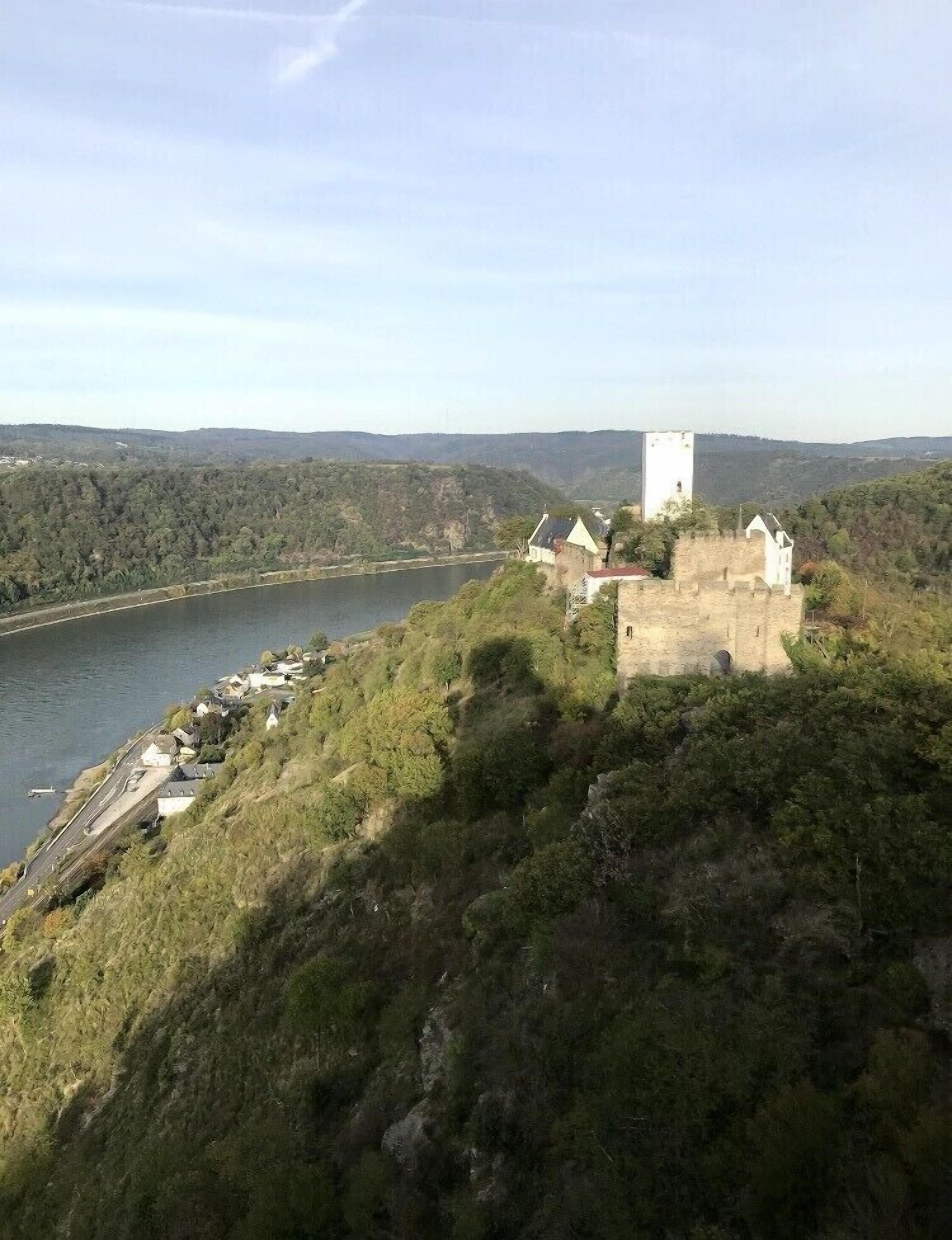 Eine schlösserartige Struktur mit einem Turm, gelegen auf einem Hügel mit Blick auf einen Fluss.