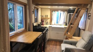 Une cuisine compacte avec un coin repas, des meubles en bois et une vue sur l’extérieur grâce à de grandes fenêtres.