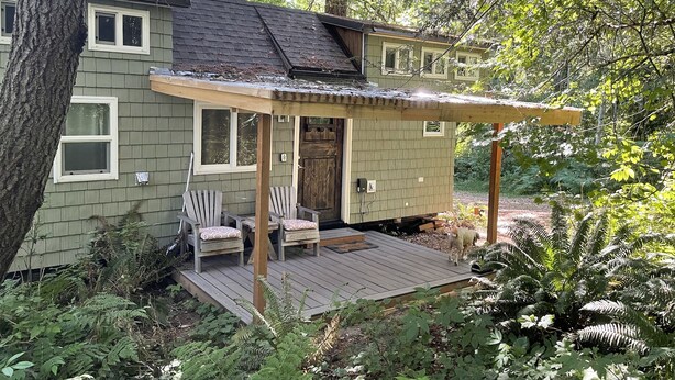 Une maison avec une terrasse, deux chaises Adirondack et un chien.