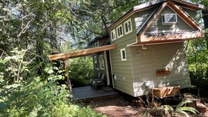 Une petite cabane à un seul étage, dotée d’un toit en pente et d’un porche, entourée d’une forêt dense.