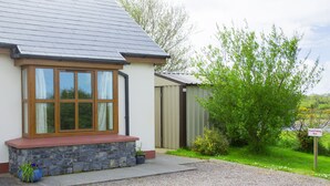 A house with a stone foundation, a red roof, and a large window with wooden frames. - Charming 1-bed Apartment in Ardfert, Tralee (Ardfert)