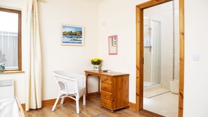 A room with a wooden desk, a wicker chair, a framed picture, and a shower area. - Charming 1-bed Apartment in Ardfert, Tralee (Ardfert)