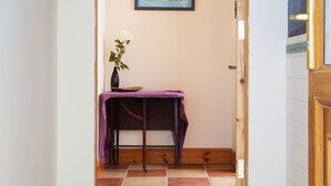 A hallway with a tiled floor, a wooden door frame, a purple table with a vase of flowers, and a framed picture on the wall. - Charming 1-bed Apartment in Ardfert, Tralee (Ardfert)