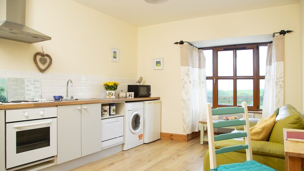 A modern kitchen with white appliances, a wooden countertop, and a view of a green couch through a window. - Charming 1-bed Apartment in Ardfert, Tralee (Ardfert)