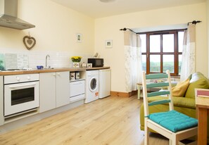 A modern kitchen with white appliances, a wooden countertop, and a view of a green couch through a window. - Charming 1-bed Apartment in Ardfert, Tralee (Ardfert)