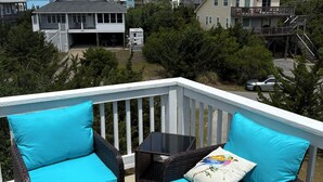 A balcony with wicker furniture and turquoise cushions, overlooking a residential area with houses and trees. - Soundside, 5 min walk to the beach, 6 private decks, shared pool and pickleball (Avon)
