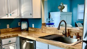 A modern kitchen with white cabinets, a stainless steel dishwasher, a wooden countertop, and a sink. - Soundside, 5 min walk to the beach, 6 private decks, shared pool and pickleball (Avon)