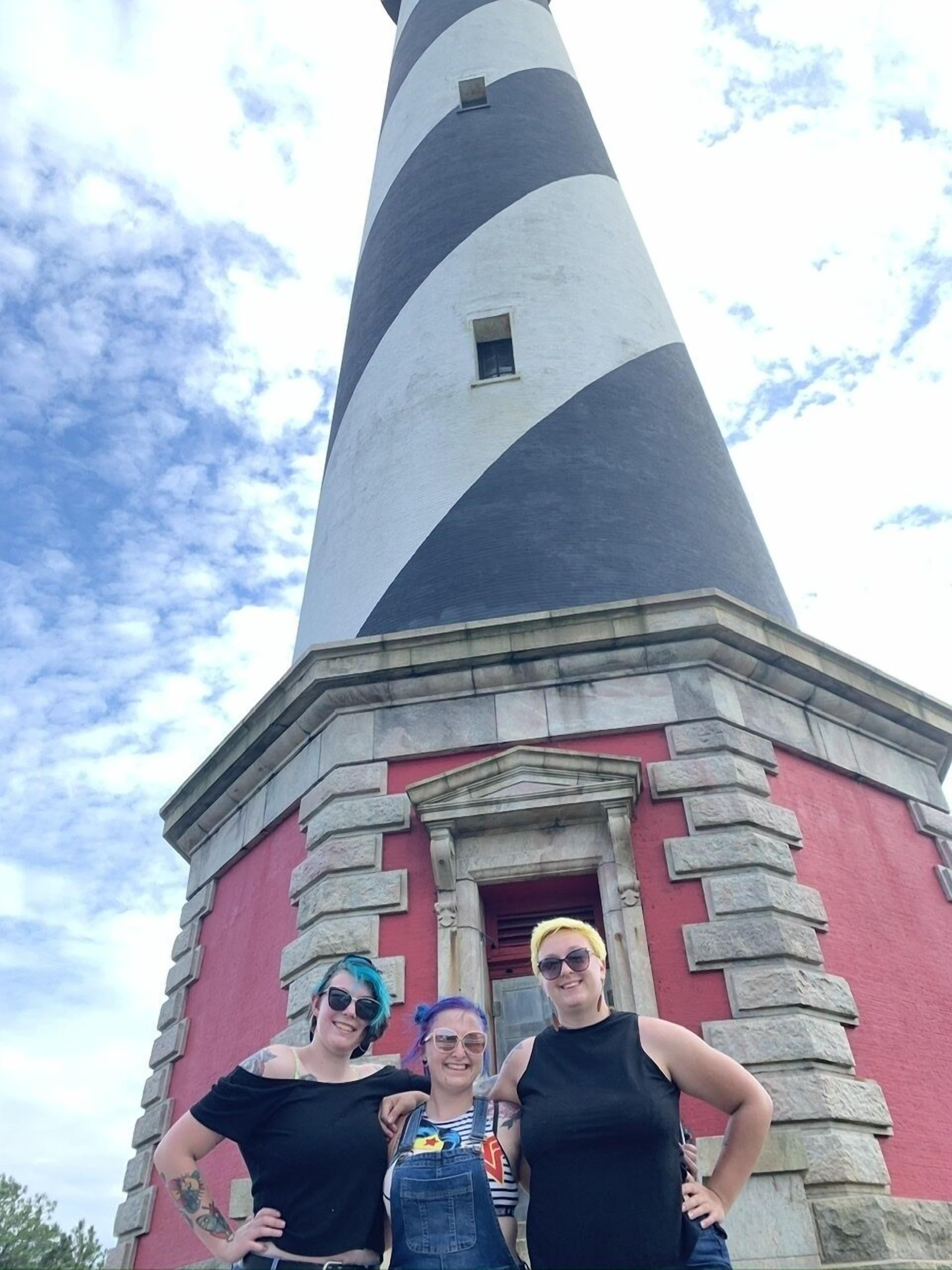 A lighthouse with a red and gray facade, a stone base, and a clear sky in the background.