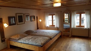 En træseng i et rum med en radiator, et vindue med gardiner og vægmonterede lamper.