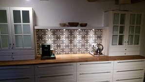 Et køkken med hvide skabe, et mønstret bagpanel og en kaffemaskine.
