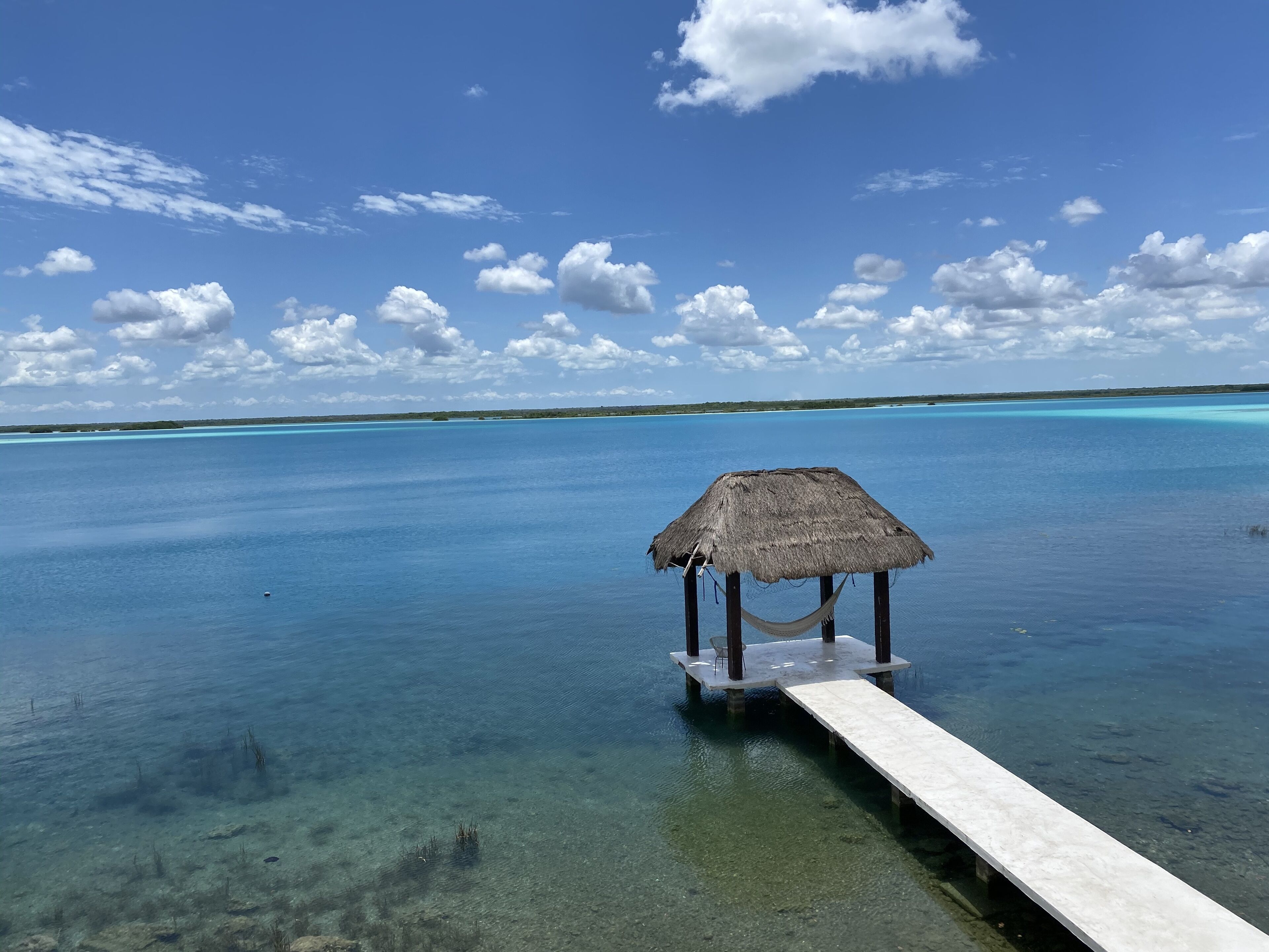 A clear blue sea with a thatched-roof structure on a pier.