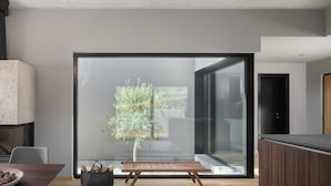A modern interior with a large sliding glass door leading to a balcony, a wooden bench, a dining table with a bowl, and a black bag on the floor. - Villa Touch of Nature with Pool (Motovun)