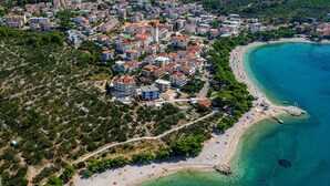 An aerial view of a coastal town with residential buildings, a beach, and clear turquoise waters. - Villa Sea Crystal with Pool (Promajna)