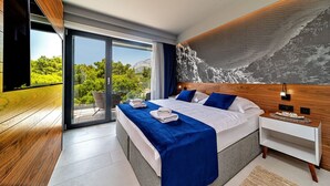 A modern bedroom with a large bed, a nightstand, and a view of greenery through a sliding glass door. - Villa Sea Crystal with Pool (Promajna)