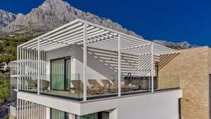 A modern two-story building with a balcony, glass railings, and outdoor seating. - Villa Sea Crystal with Pool (Promajna)