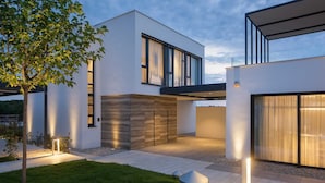 Une maison moderne à deux étages, dotée de grandes fenêtres et d’un toit plat.