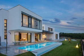 A modern two-story house with a swimming pool, outdoor seating, and a well-maintained lawn.