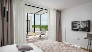 Une chambre d’hôtel moderne dotée d’un grand lit, d’un balcon avec vue et d’un téléviseur à écran plat fixé au mur.