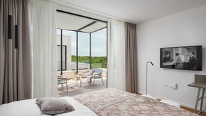 Une chambre d’hôtel moderne avec un grand lit, un balcon doté d’une table et de chaises, et un téléviseur fixé au mur.